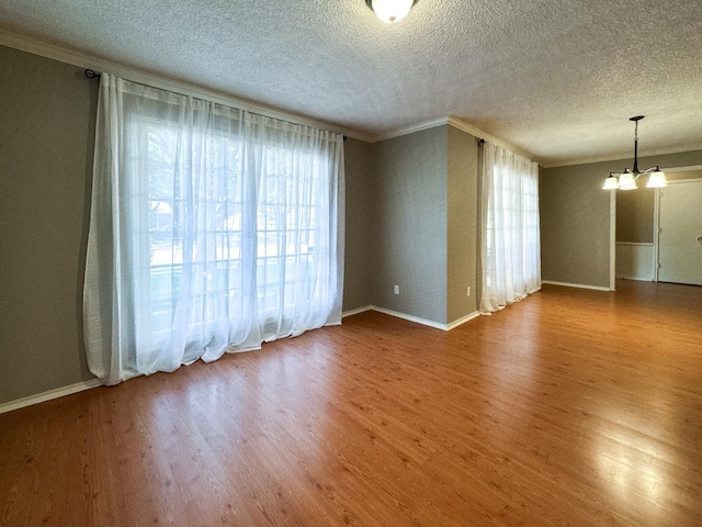 empty room with crown molding, wood-type flooring, a textured ceiling, and a notable chandelier