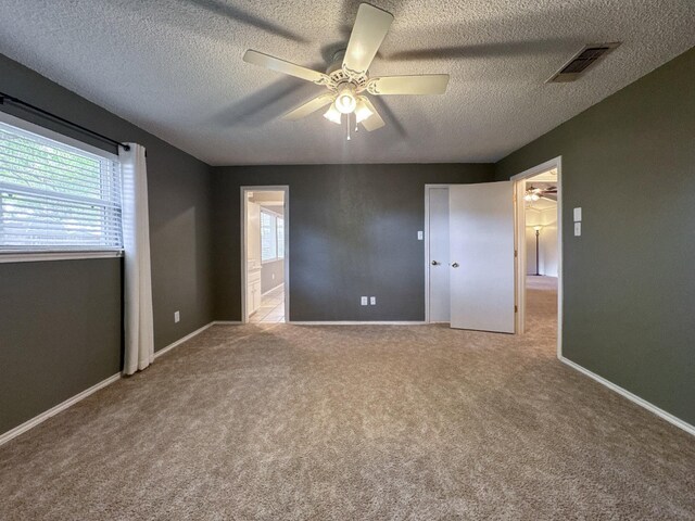 unfurnished bedroom featuring multiple windows, ceiling fan, light colored carpet, and a textured ceiling