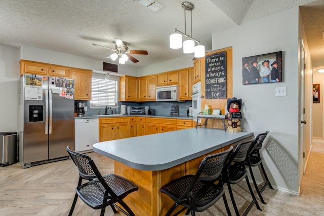 kitchen with sink, white appliances, a breakfast bar, hanging light fixtures, and kitchen peninsula