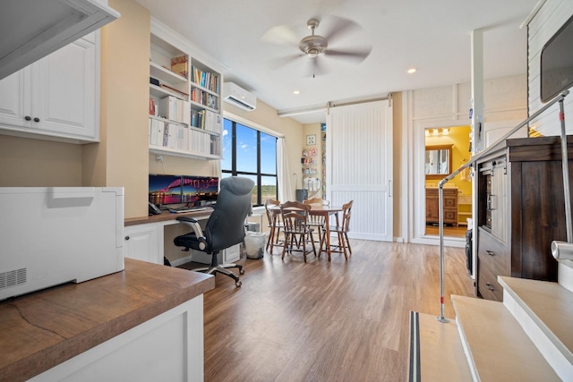 office with ceiling fan, wood-type flooring, built in desk, and a wall unit AC