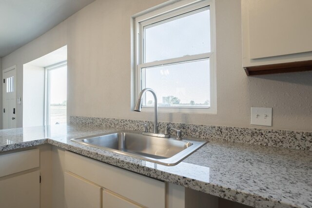 kitchen with white cabinetry, a healthy amount of sunlight, sink, and light stone counters