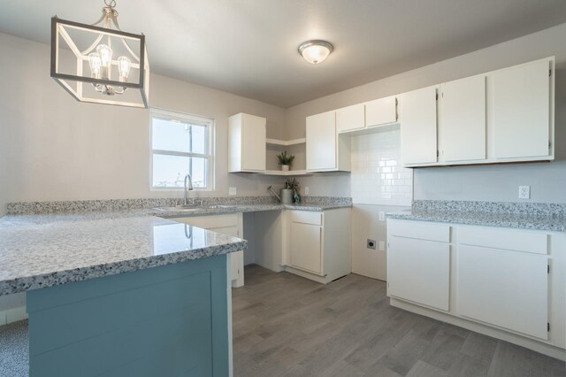 kitchen featuring sink, light hardwood / wood-style flooring, light stone counters, white cabinets, and decorative light fixtures