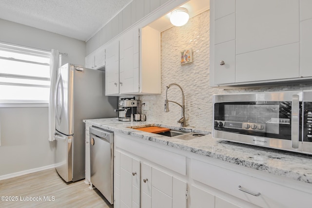 4816 55th St, Lubbock, TX 79414 - kitchen with appliances with stainless steel finishes, a sink, tasteful backsplash, white cabinets, and light wood-type flooring