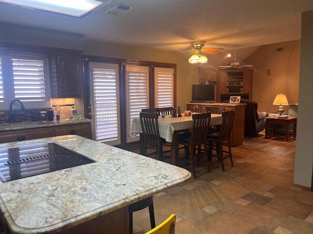 kitchen featuring ceiling fan, light stone countertops, sink, and black stovetop