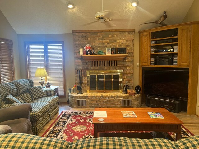 living room featuring vaulted ceiling, ceiling fan, a fireplace, and light hardwood / wood-style flooring