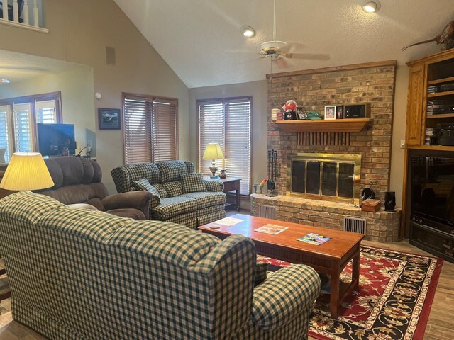 living room with hardwood / wood-style flooring, ceiling fan, high vaulted ceiling, and a brick fireplace