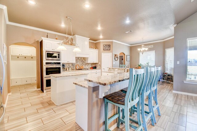 kitchen featuring a large island, appliances with stainless steel finishes, light stone countertops, white cabinets, and decorative backsplash