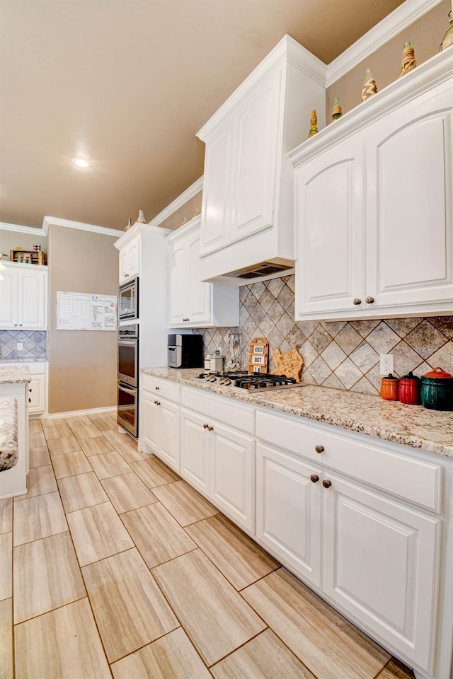 kitchen featuring light stone counters, stainless steel appliances, crown molding, and white cabinets