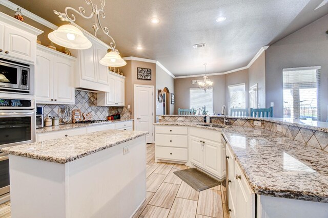 kitchen with sink, hanging light fixtures, stainless steel appliances, white cabinets, and a kitchen island