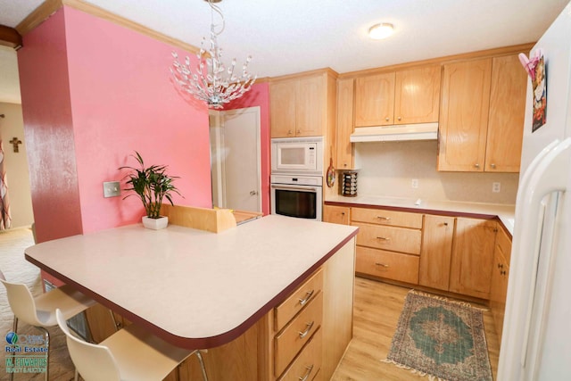kitchen with under cabinet range hood, white appliances, light countertops, hanging light fixtures, and light wood finished floors