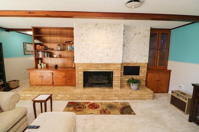 living area with built in shelves, a fireplace, wainscoting, light carpet, and beamed ceiling