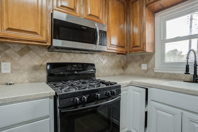 kitchen with tasteful backsplash, black gas stove, sink, and white cabinets