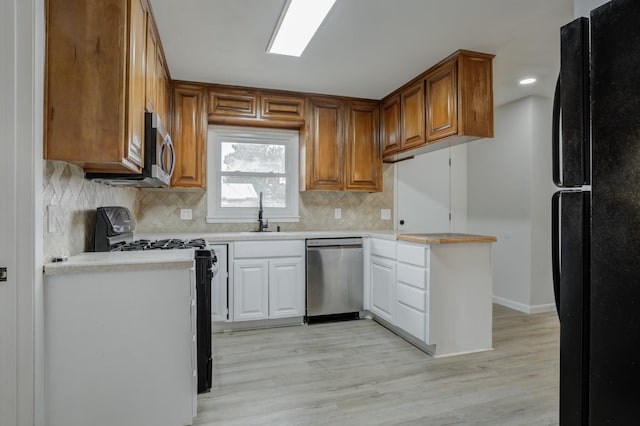 kitchen with tasteful backsplash, sink, light hardwood / wood-style flooring, and black appliances