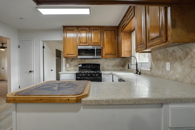 kitchen with decorative backsplash, sink, black range with gas stovetop, and kitchen peninsula