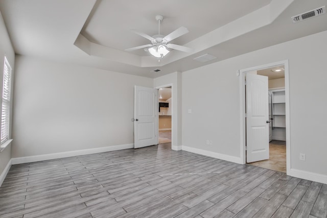 unfurnished bedroom featuring a closet, a walk in closet, a raised ceiling, and ceiling fan