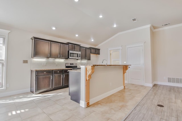 kitchen with appliances with stainless steel finishes, lofted ceiling, backsplash, ornamental molding, and a center island with sink