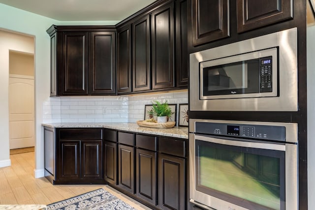 kitchen with stainless steel appliances, dark brown cabinetry, tasteful backsplash, light stone countertops, and light hardwood / wood-style floors