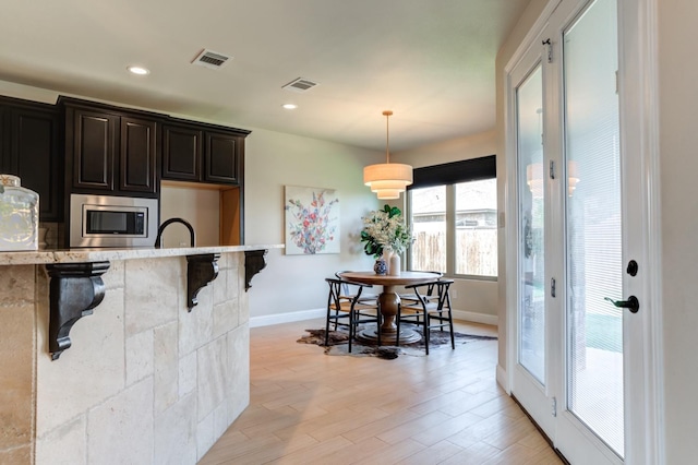 kitchen featuring a breakfast bar, stainless steel microwave, light wood-type flooring, and decorative light fixtures