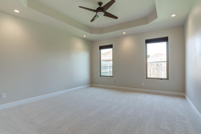 carpeted empty room featuring ceiling fan, a tray ceiling, and a wealth of natural light