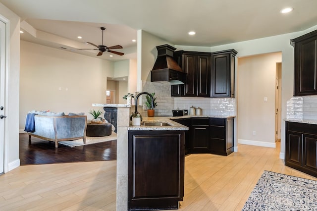 kitchen with sink, premium range hood, backsplash, light stone counters, and light wood-type flooring