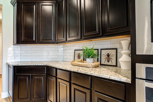 kitchen featuring light stone countertops, dark brown cabinetry, oven, and decorative backsplash