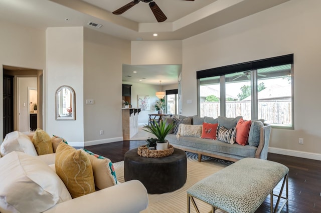 living room with a high ceiling, a raised ceiling, dark hardwood / wood-style floors, and a wealth of natural light