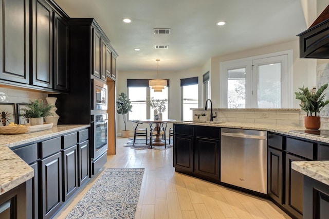 kitchen with appliances with stainless steel finishes, pendant lighting, sink, backsplash, and light wood-type flooring