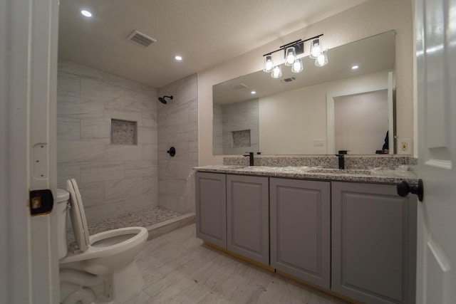 bathroom featuring vanity, a tile shower, and toilet