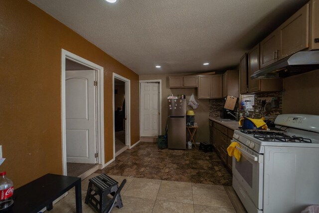 kitchen featuring sink, white gas stove, tasteful backsplash, a textured ceiling, and stainless steel fridge