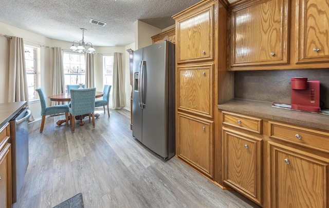 kitchen featuring an inviting chandelier, light wood finished floors, brown cabinets, and stainless steel appliances