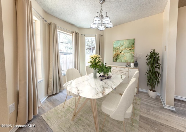 dining space featuring light wood-style floors, baseboards, a textured ceiling, and a chandelier
