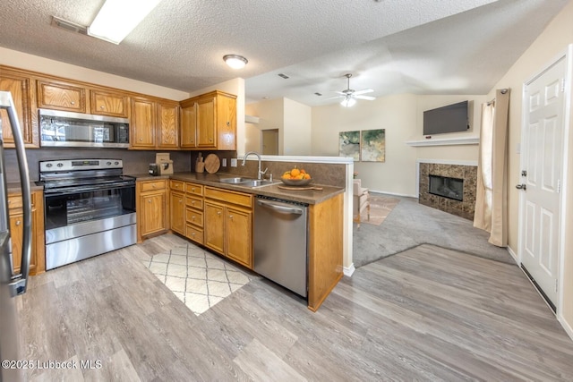 kitchen with open floor plan, ceiling fan, a sink, light wood-style flooring, and appliances with stainless steel finishes
