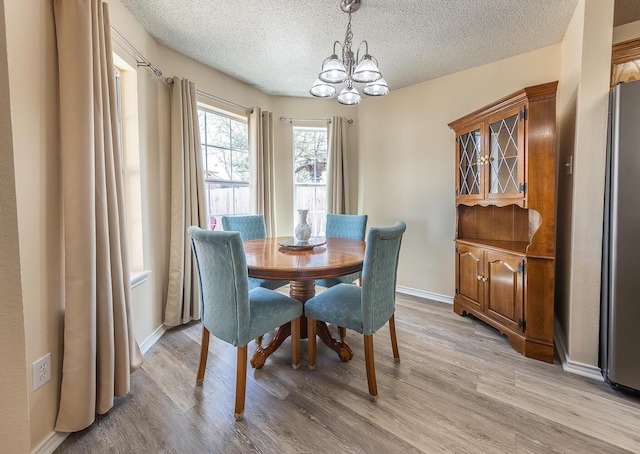 dining room with an inviting chandelier, a textured ceiling, baseboards, and light wood-type flooring