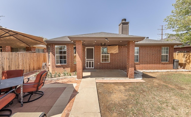 back of property with brick siding, fence, a chimney, and a patio area