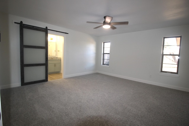 unfurnished bedroom with a barn door, a ceiling fan, light carpet, ensuite bath, and baseboards