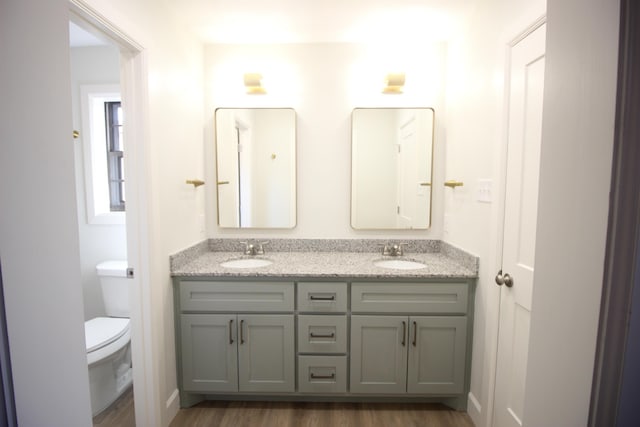 bathroom featuring wood finished floors, a sink, toilet, and double vanity