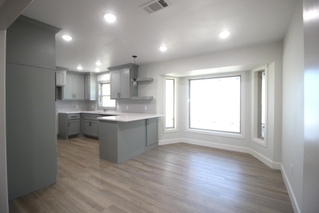 kitchen with tasteful backsplash, gray cabinets, visible vents, wood finished floors, and a peninsula