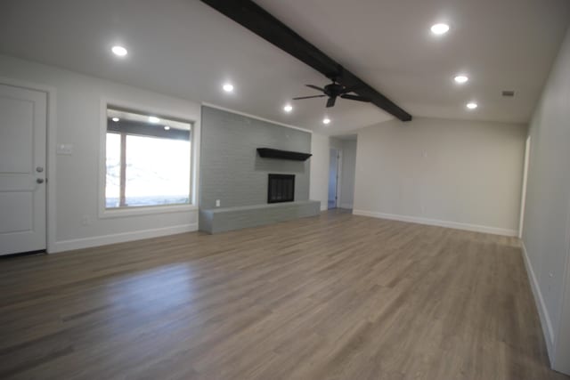 unfurnished living room featuring vaulted ceiling with beams, a fireplace, wood finished floors, a ceiling fan, and baseboards