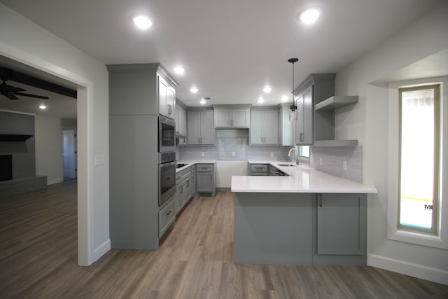 kitchen with wood finished floors, a peninsula, stainless steel appliances, gray cabinetry, and open shelves