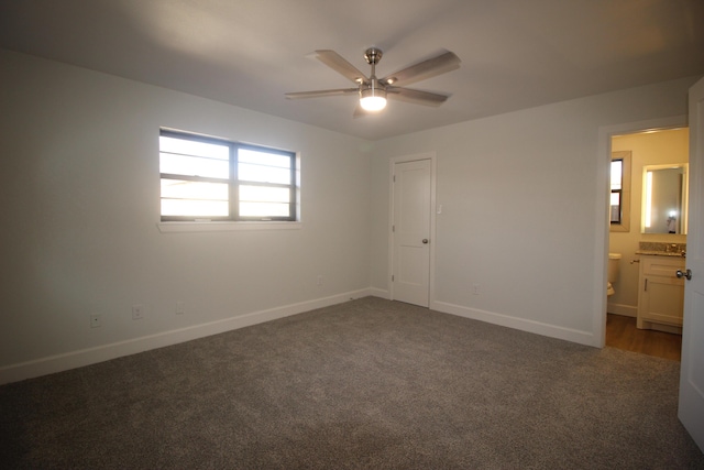 unfurnished bedroom with a ceiling fan, dark colored carpet, connected bathroom, and baseboards