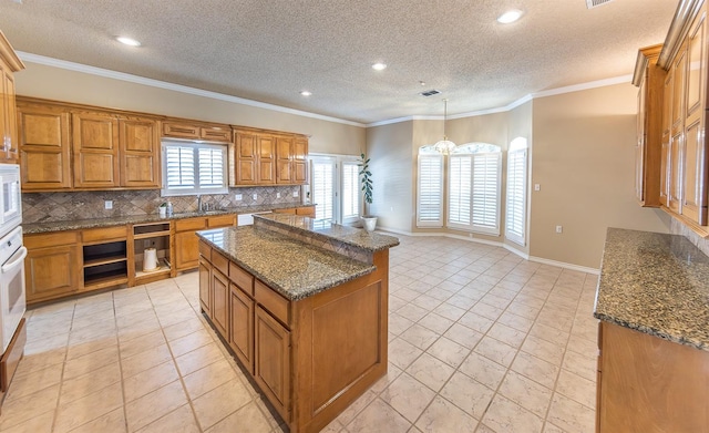 kitchen with a kitchen island, decorative light fixtures, tasteful backsplash, dark stone countertops, and crown molding