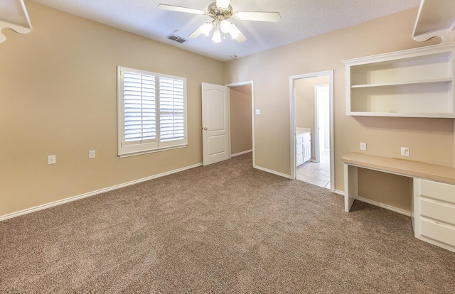 unfurnished bedroom with ceiling fan, light colored carpet, built in desk, and a textured ceiling