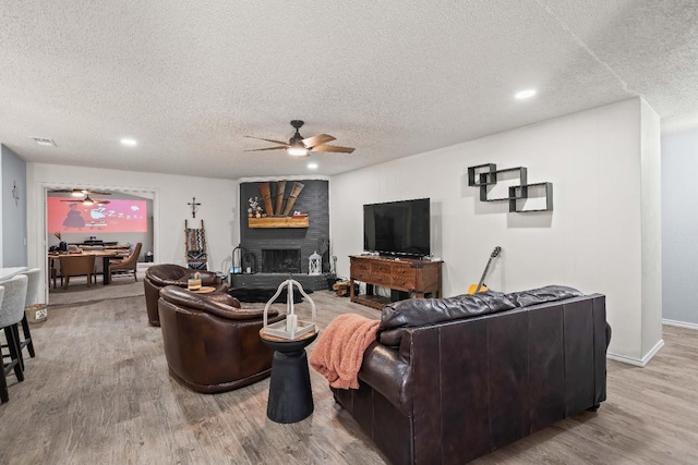 living room featuring ceiling fan, a large fireplace, light hardwood / wood-style floors, and a textured ceiling