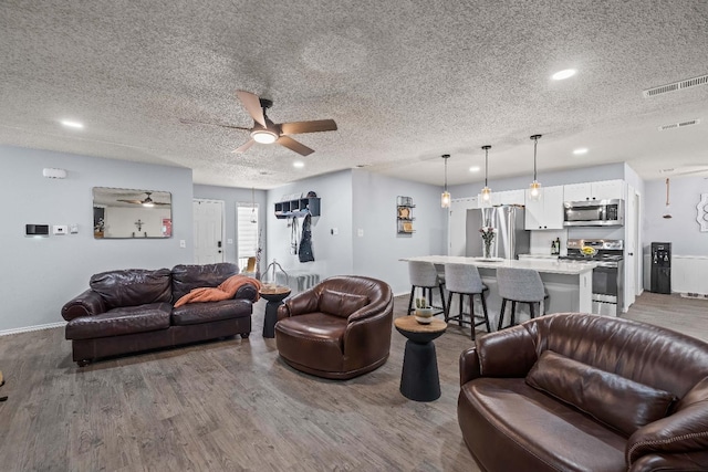 living room with ceiling fan, hardwood / wood-style flooring, and a textured ceiling