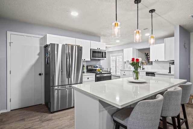 kitchen featuring pendant lighting, stainless steel appliances, a center island, and white cabinets