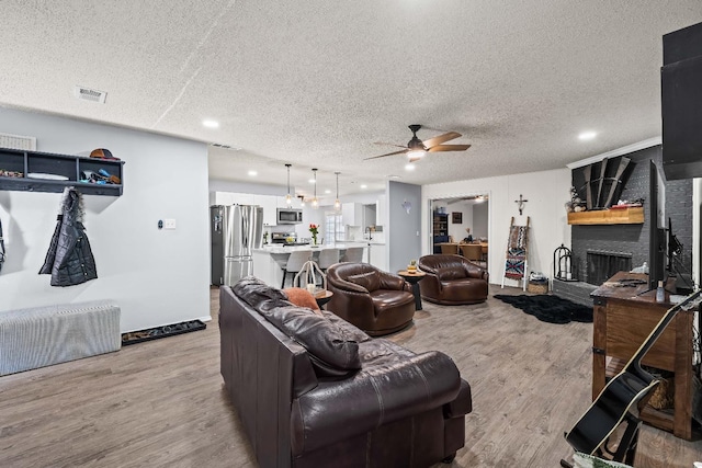 living room with a fireplace, a textured ceiling, light hardwood / wood-style flooring, and ceiling fan