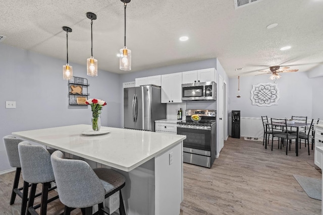 kitchen with a kitchen island, appliances with stainless steel finishes, pendant lighting, white cabinetry, and light hardwood / wood-style floors