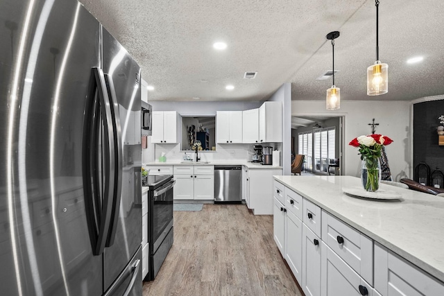 kitchen featuring pendant lighting, sink, stainless steel appliances, light stone countertops, and white cabinets