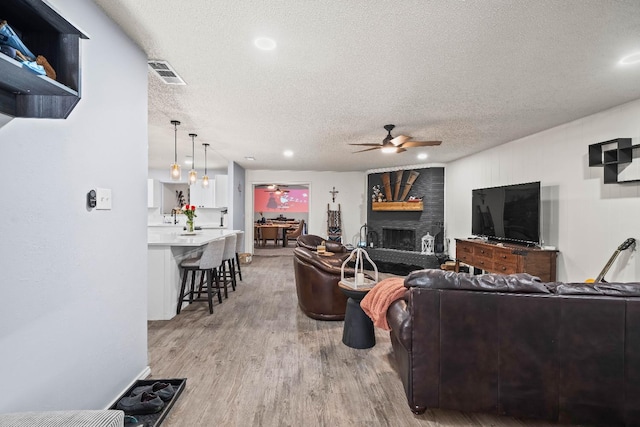 living room with hardwood / wood-style floors, a textured ceiling, a large fireplace, and ceiling fan