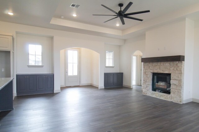 unfurnished living room with baseboards, visible vents, dark wood-style floors, a tray ceiling, and a fireplace